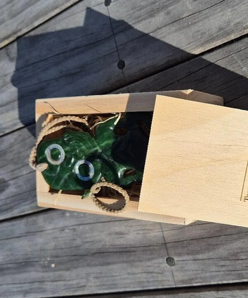Carved pounamu pendant with shell inlay eyes in a wooden gift box by Taonga by Timoti