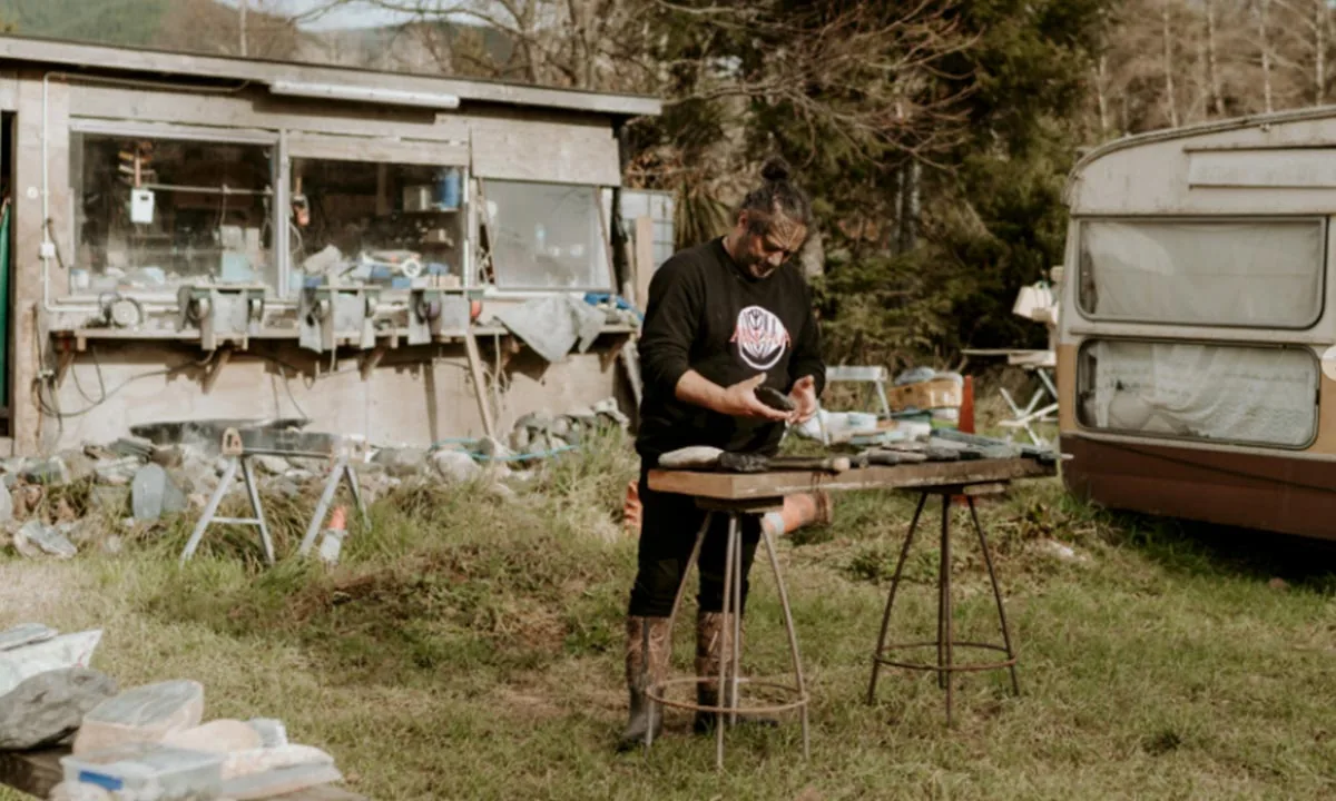 Pounamu carver shaping stone at an outdoor workbench beside the Taonga by Timoti workshop near Nelson