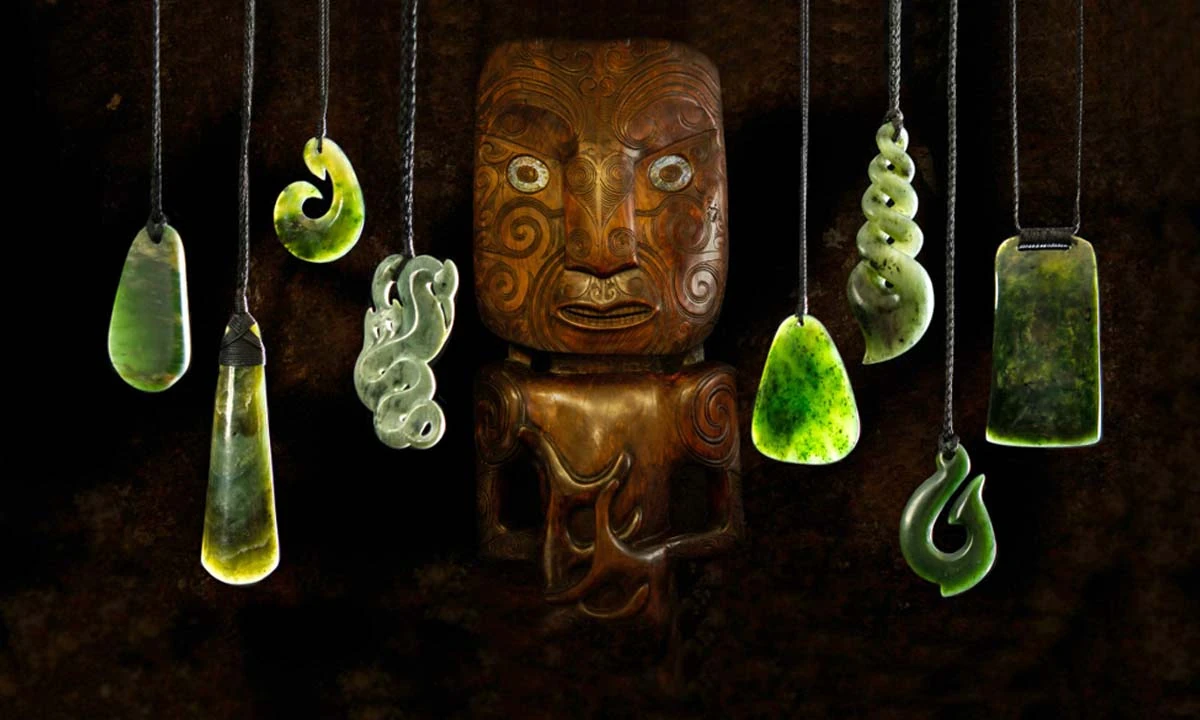 Pounamu pendants including a koru, twist, hei matau and toki hung either side of a carved wooden Māori figure