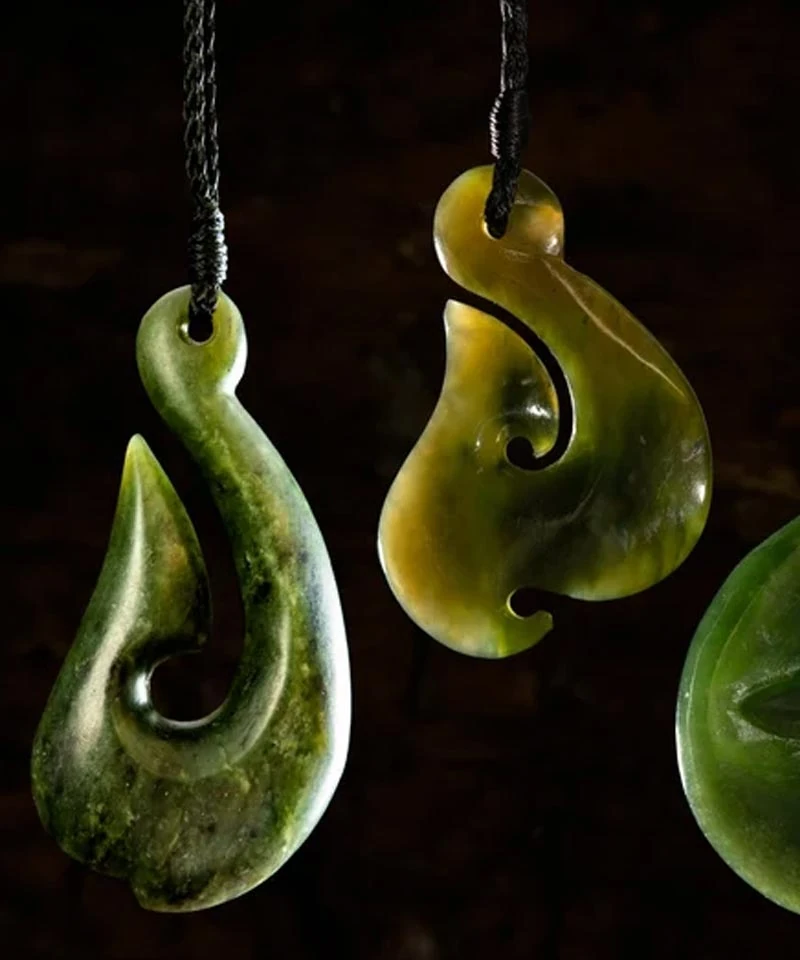 Two hand carved pounamu pendants, a hei matau fish hook and a flowing koru design, at Greenstone Shop Christchurch