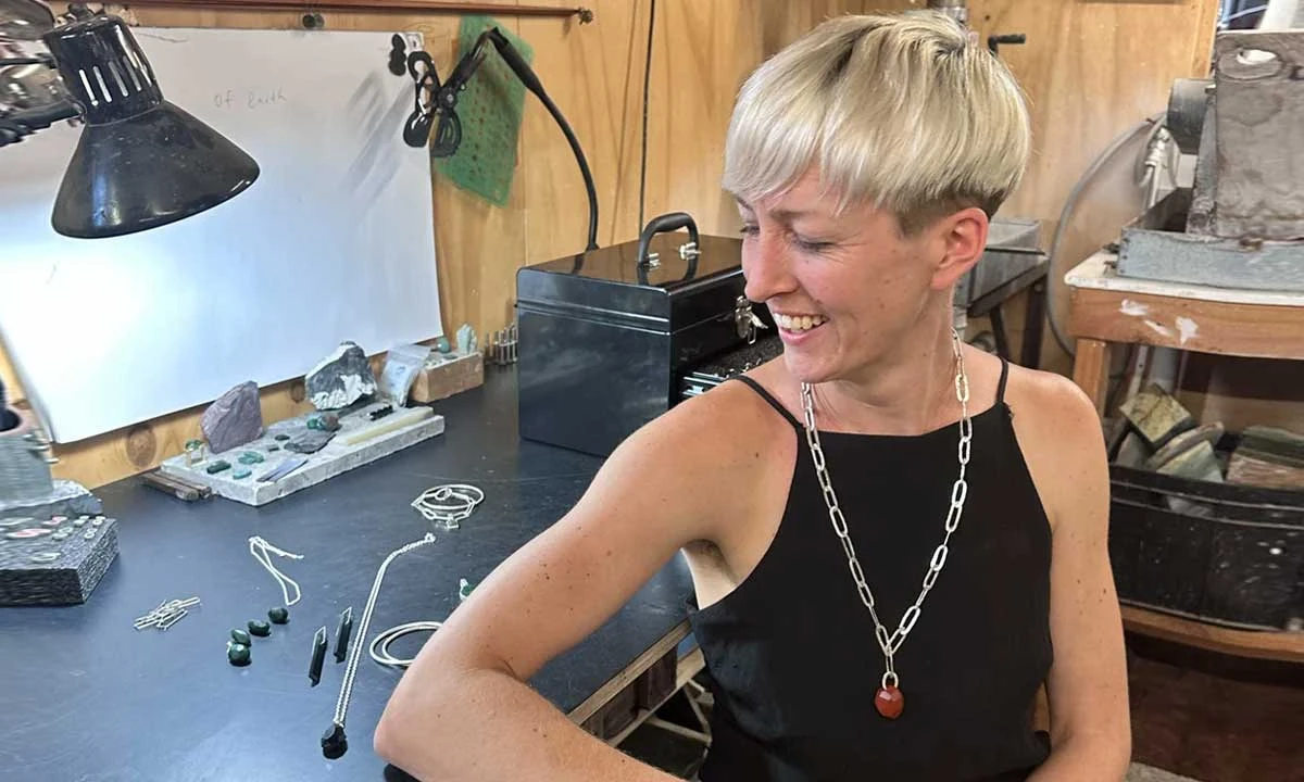 Jeweller Hannah Sheehan at her Auckland workbench with pounamu pieces, silver chains and raw stone offcuts