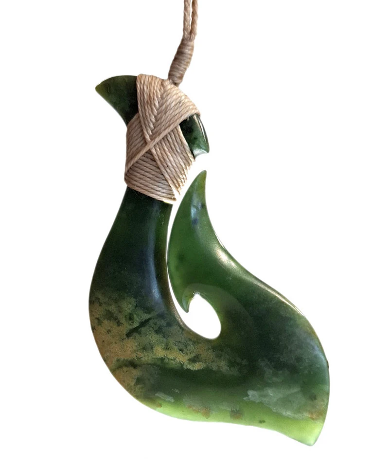 Hand carved pounamu hei matau fish hook with a tan cord lashing, sold at Hokitika Craft Gallery