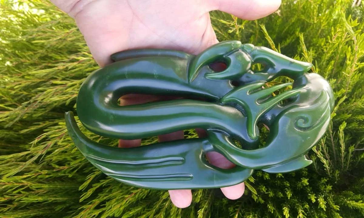 Large flowing pounamu carving with a bird-like head and koru detail held in a hand, by Jade Art Carvings, Hokitika