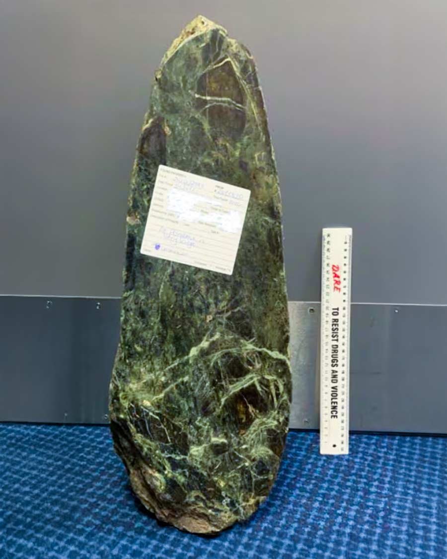 The mystery pounamu slab found near Te Kaha, shown with a police evidence tag and ruler for scale