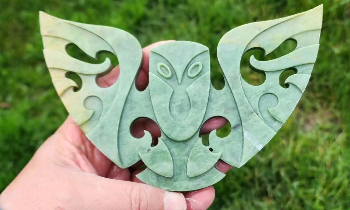 Large pale green jade carving of an owl-like figure with outstretched wings, held in a hand, by Kerry Thompson