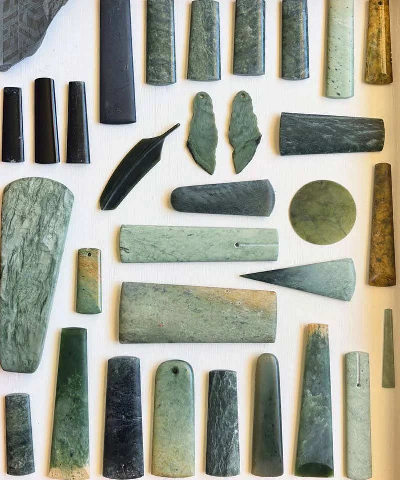 Polished jade toki, feather, leaf and disc pendants in many shades of green and black, laid out by Thompson Carvers