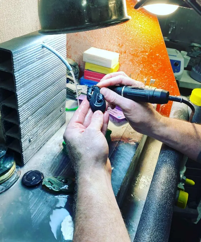 Carver shaping a dark stone pendant with a rotary tool at the Wai Kaha Pounamu workbench in Christchurch