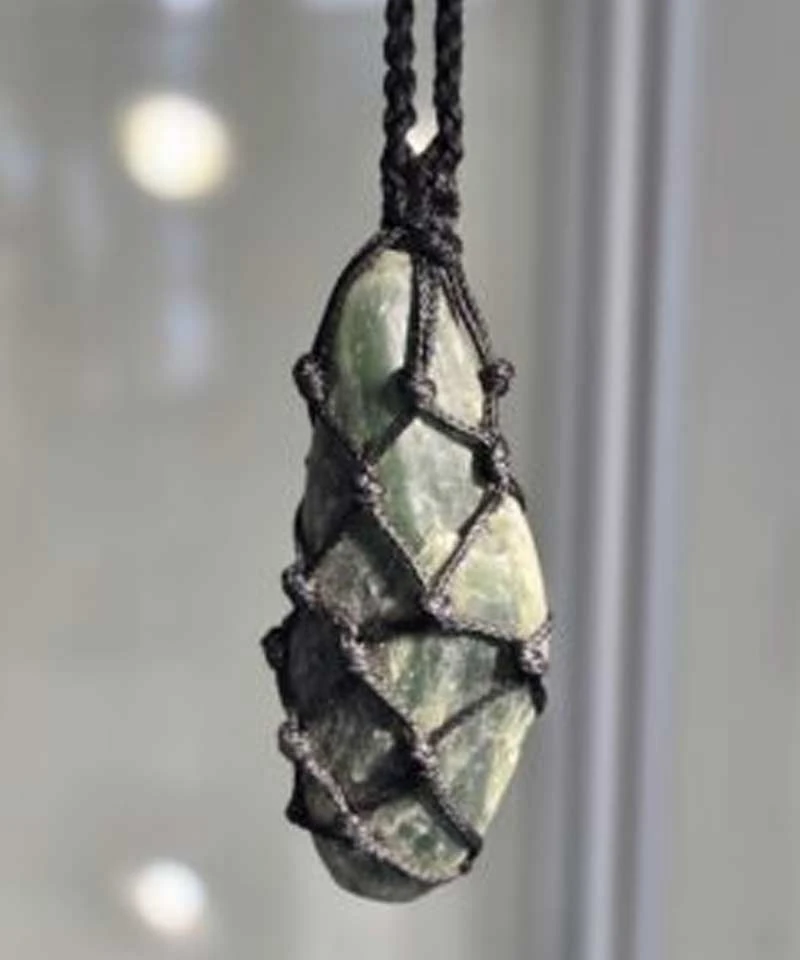 Natural pounamu stone held in a knotted black cord net, from Wai Kaha Pounamu in Ferrymead