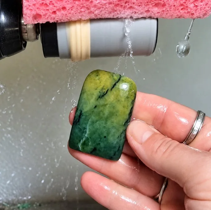 Pounamu hei toki being shaped under water on a wet sanding wheel in the Your PRANA workshop