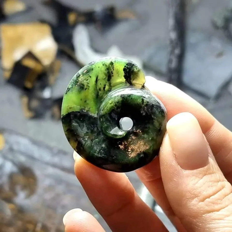 Green stone disc carving by Your PRANA held between fingers, showing dark inclusions and bright green colour